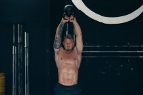 Determined male athlete with naked torso doing kettlebell snatch exercise during functional workout in gym — Stock Photo