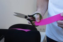 Masculino fisioterapeuta en mascarilla estéril cortando cinta cinesiológica elástica con tijeras en el hospital - foto de stock
