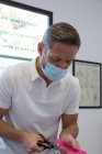 Physiothérapeute masculin attentif anonyme en masque stérile coupant la bande élastique de kinésiologie avec des ciseaux à l'hôpital — Photo de stock