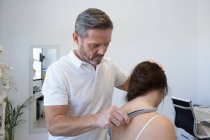Чоловічий фізіотерапевт масажує спину анонімної топлес жінки з інструментом з нержавіючої сталі в клініці — стокове фото