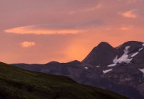 Vista mozzafiato di maestose montagne accidentate con neve su pendii vicino alla valle collinare erbosa sotto il pittoresco cielo rosa serale in Islanda — Foto stock