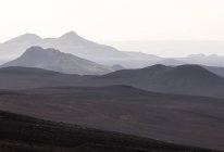Живописный пейзаж грубого горного хребта с вершинами в густом тумане под мрачным небом в высокогорье — стоковое фото