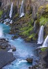 Espectacular vista de las rápidas cascadas que fluyen desde el áspero acantilado rocoso cubierto de exuberante vegetación hacia el tranquilo embalse azul en naturaleza pacífica - foto de stock
