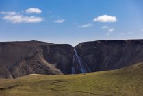 Дивовижний краєвид зеленої горбистої місцевості з швидким каскадом, що тече з скелястого грубого гірського хребта — стокове фото