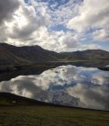 Paesaggio mozzafiato di lago ancora tranquillo che riflette il cielo azzurro e circondato da colline rocciose verdi in altopiani pacifici in Islanda — Foto stock