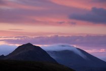 Panorama mozzafiato della catena montuosa rocciosa con cime nella densa nebbia sotto il maestoso cielo rosa al tramonto — Foto stock