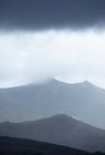Paysage pittoresque d'une chaîne de montagnes rugueuse avec des pics dans un brouillard dense sous un ciel sombre et nuageux dans les hautes terres — Photo de stock