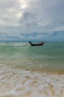 Paysage paisible d'un petit bateau amarré sur des ondulations d'eau de mer azur sous un ciel nuageux et sombre dans un pays tropical — Photo de stock