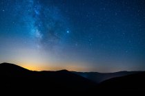 Живописный вид звездно-синего неба с облаками над горой с силуэтами гор на закате — стоковое фото