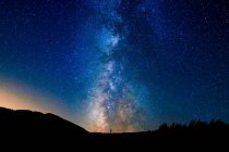 Мальовничий вид на зоряне блакитне небо з хмарами над горою з невизначеними силуетами людини на заході сонця — стокове фото