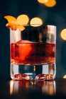 Bicchiere di rinfrescante cocktail alcolico Negroni guarnito con buccia d'arancia matura e messo in tavola tra gli attrezzi da barman — Foto stock