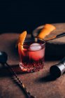 Bicchiere di rinfrescante cocktail alcolico Negroni guarnito con buccia d'arancia e messo in tavola tra gli attrezzi da barman — Foto stock