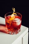 Склянка гіркого алкогольного негритянського коктейлю, подається з льодом та апельсиновою шкіркою на білій поверхні — стокове фото