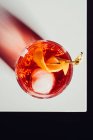 Бокал горького алкогольного коктейля Негрони подается со льдом и апельсиновой кожурой на белой поверхности — стоковое фото