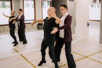 Seitenansicht des männlichen Instruktors hilft reifen Tänzern bei der Bewegung während des Standardtanzes im geräumigen Saal — Stockfoto