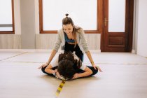 Alegre instructora femenina ayudando a chica flexible con piernas estiradas antes de bailar en el estudio - foto de stock