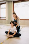 Веселая женщина-инструктор помогает гибкой девушке с растянутыми ногами перед танцами в студии — стоковое фото