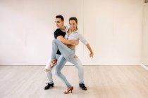 Содержание квалифицированной пары, исполняющей бальные танцы во время урока в светлом просторном зале и смотрящей в сторону — стоковое фото