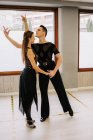 Slender graceful couple performing ballroom dance while rehearsing in bright studio and holding hands — Stock Photo
