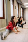 Lächelnde Trainerin in Sportbekleidung hilft fröhlichem Mädchen mit streckenden Beinen beim Aufwärmen vor dem Fitnesstraining — Stockfoto