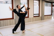 Skilled couple of dancers in elegant clothes rehearsing moves of ballroom dance during class in studio — Stock Photo
