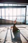 Seitenansicht einer Theaterkünstlerin, die mit erhobenem Arm tanzt und auf den Boden blickt, mit Schatten gegen Glaswand — Stockfoto