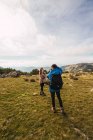 Trekker masculin méconnaissable prenant une photo du partenaire féminin sur la caméra alors qu'il se tenait debout sur la pelouse contre le mont sous un ciel nuageux — Photo de stock