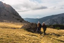 Meilleures amies méconnaissables en vêtements de dessus se promenant sur le mont avec de l'herbe pendant le voyage en Espagne — Photo de stock