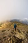 From above back view of anonymous male trekker with rucksack standing on pathway against mount on misty day — Stock Photo