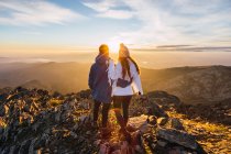 Vista posterior de una pareja anónima de turistas admirando majestuosas montañas bajo un cielo brillante a la luz del sol - foto de stock