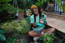Посміхаючись, чорна жінка - садівник сидить на землі в хатині і пересаджує квітку Каланчоу. — стокове фото