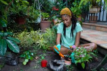 Lächelnde schwarze Gärtnerin sitzt im Gewächshaus auf dem Boden und verpflanzt Kalanchoe-Blume — Stockfoto