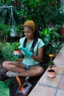 Hippie fêmea preta com dreadlocks jardineiro sentado na estufa e plantio de plantas verdes em vasos cerâmicos — Fotografia de Stock