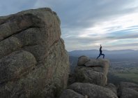 Vista laterale di donna irriconoscibile in piedi sulla cima di una montagna rocciosa e facendo Warrior una posa durante il tramonto — Foto stock