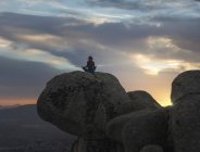 Задний вид неузнаваемой спокойной женщины, выполняющей упражнения йоги, практикующей медиацию на каменистой земле на ярком закате — стоковое фото