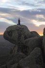 Задний вид неузнаваемой спокойной женщины, выполняющей упражнения йоги, практикующей медиацию на каменистой земле на ярком закате — стоковое фото
