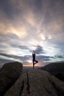 Back view of unrecognizable female standing on top of rocky mountain and doing Tree with Arms Up pose during sunset — Stock Photo