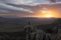 Вид ззаду на невпізнавану жінку, що стоїть на вершині скелястої гори і робить позу гори під час заходу сонця — стокове фото