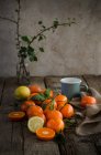 Стиглі мандарини і лимон, розташовані на дерев'яному столі з чашкою і серветкою, підготовленою для приготування мусу — стокове фото