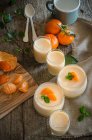 Alto ângulo de mousse de tangerina saborosa decorada com folhas de hortelã frescas servidas em copos de vidro na mesa de madeira — Fotografia de Stock