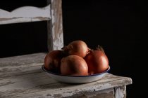 Bowl with whole unpeeled onions placed on shabby wooden chair — Stock Photo
