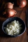 Vue du dessus du bol rustique avec des morceaux d'oignon coupé placés près du couteau sur la table à bois dans la cuisine — Photo de stock