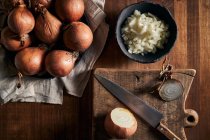 Draufsicht auf rustikale Schüssel mit geschnittenen Zwiebelstücken, die in der Nähe des Messers auf dem Holztisch in der Küche platziert werden — Stockfoto