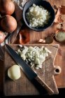 Vue du dessus du bol rustique avec des morceaux d'oignon coupé placés près du couteau sur la table à bois dans la cuisine — Photo de stock