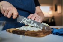 Erntefrau in Schürze schneidet rohe Zwiebel auf Schneidebrett auf dem Tisch in der heimischen Küche — Stockfoto