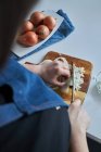 Crop donna in grembiule tritare cipolla cruda sul tagliere sul tavolo in cucina a casa — Foto stock