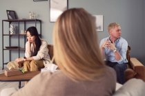 Multiethnic couple sitting on couch and talking about mental problems during therapy session with psychologist — Stock Photo