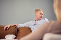 Homem preocupado sentado no sofá e falando durante a sessão de psicoterapia mental com o psicólogo — Fotografia de Stock