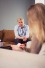 Занепокоєний чоловік сидить на дивані і виступає під час сеансу психотерапії з психологом — стокове фото