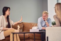 Мультиэтническая пара сидит на диване и говорит о психических проблемах во время сеанса терапии с психологом — стоковое фото